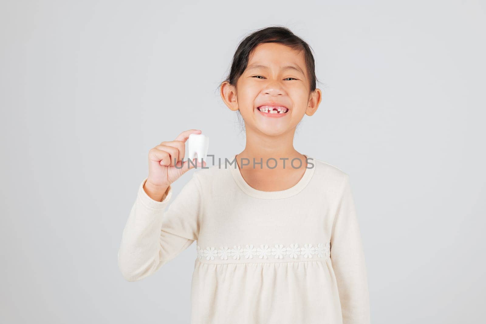 Dentist explains tooth loss to happy girl, showing her mouth gap and tooth model. Child smiling with missing teeth, learning dental care and healthy teeth habits. isolated white background