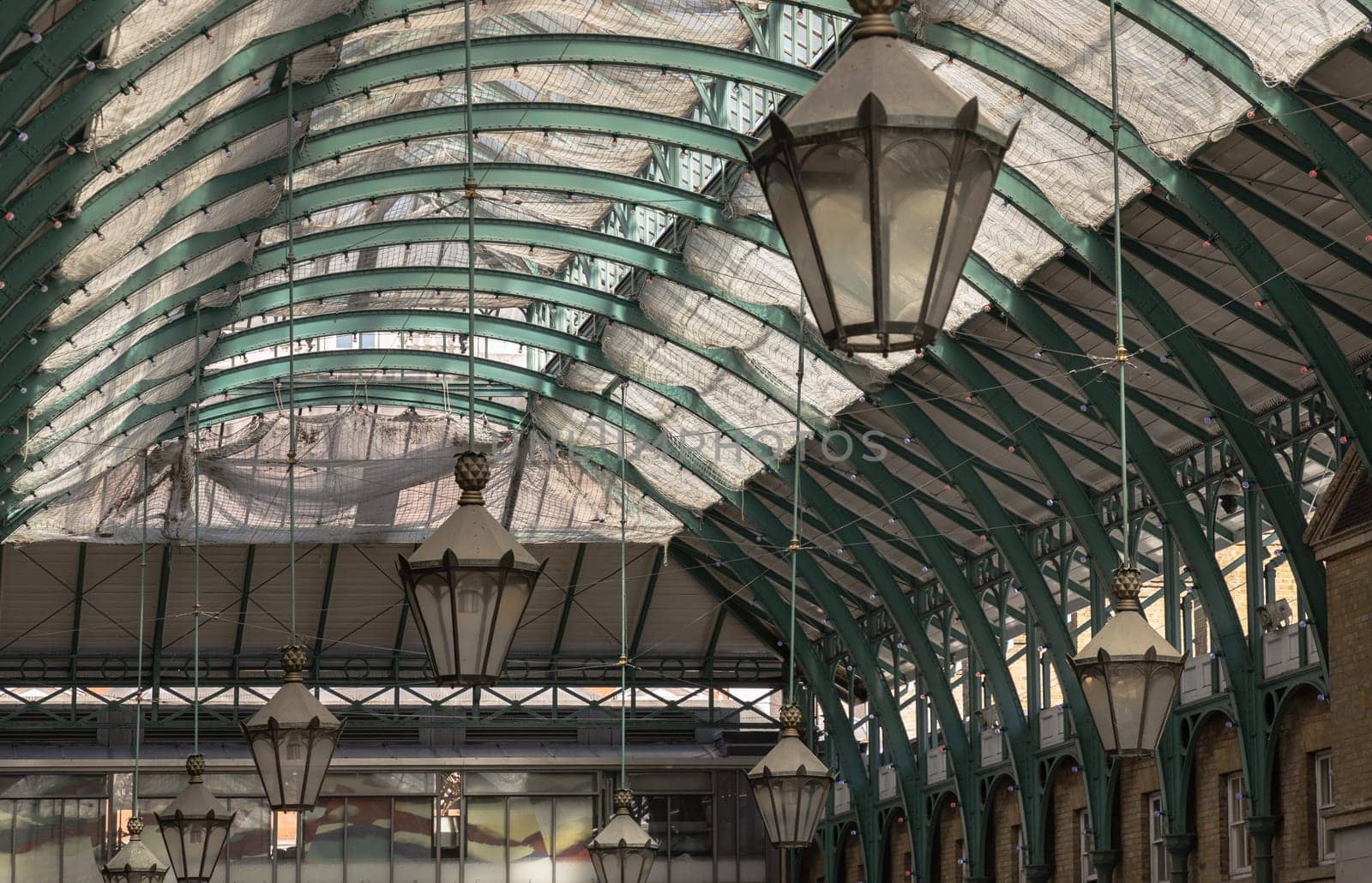 London, UK - May 13, 2025 - Architecture greco-roman style with iron glass roof and Lanterns hanging on the ceiling in Covent Garden Market Hall. View of Metallic framework arch roof with ceiling hanging lamp, use it as your Wallpaper, Poster and Space for text, Selective focus.
