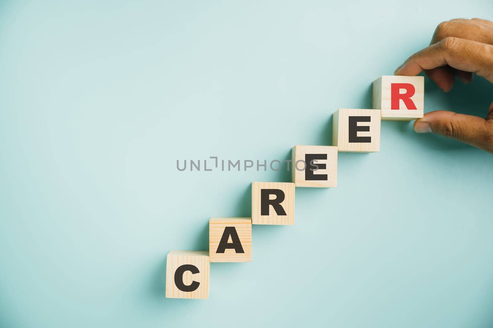 Career planning and growth. A hand places a wooden cube block labeled CAREER on a vibrant blue background, offering copy space for text and emphasizing the significance of business success.