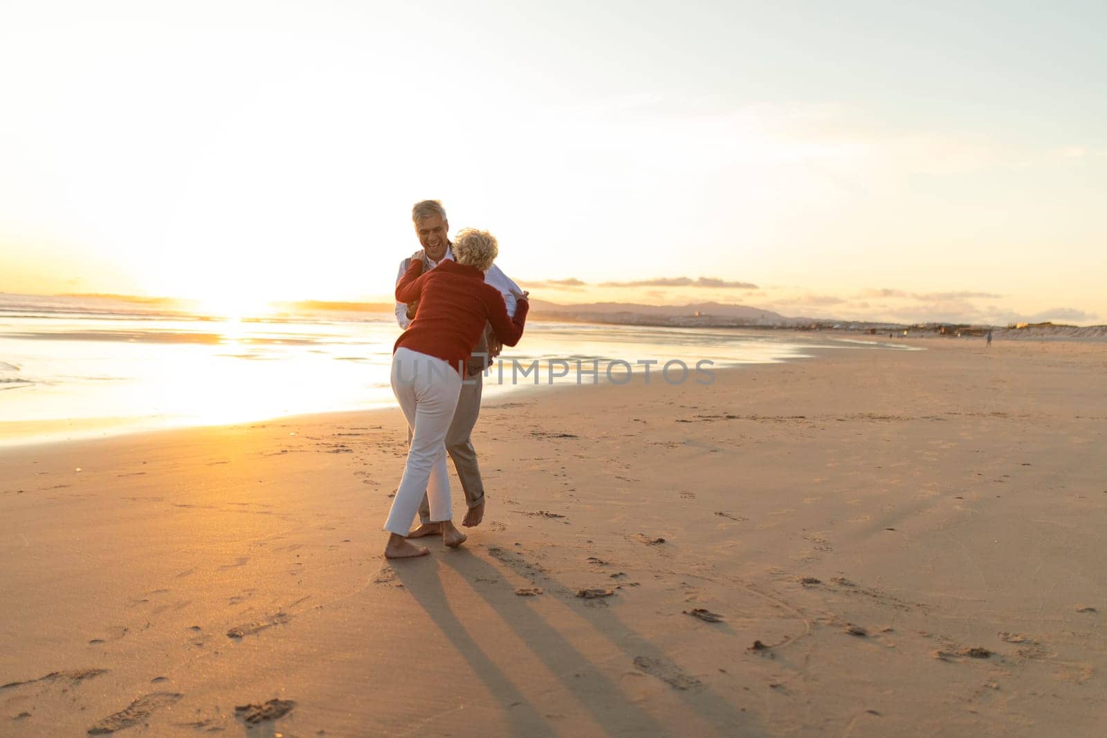 Happy retired couple dancing together on the beach at sunset
