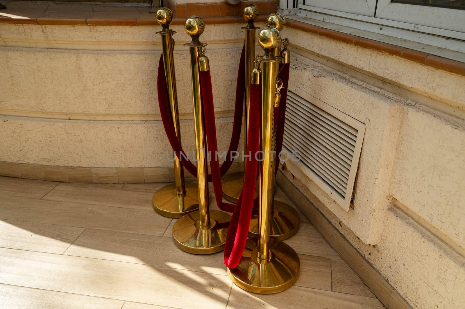 Gold colored metal stanchions with red velvet rope for crowd control. A group of red velvet ropes and gold poles on the street, waiting to be installed near the hotel building