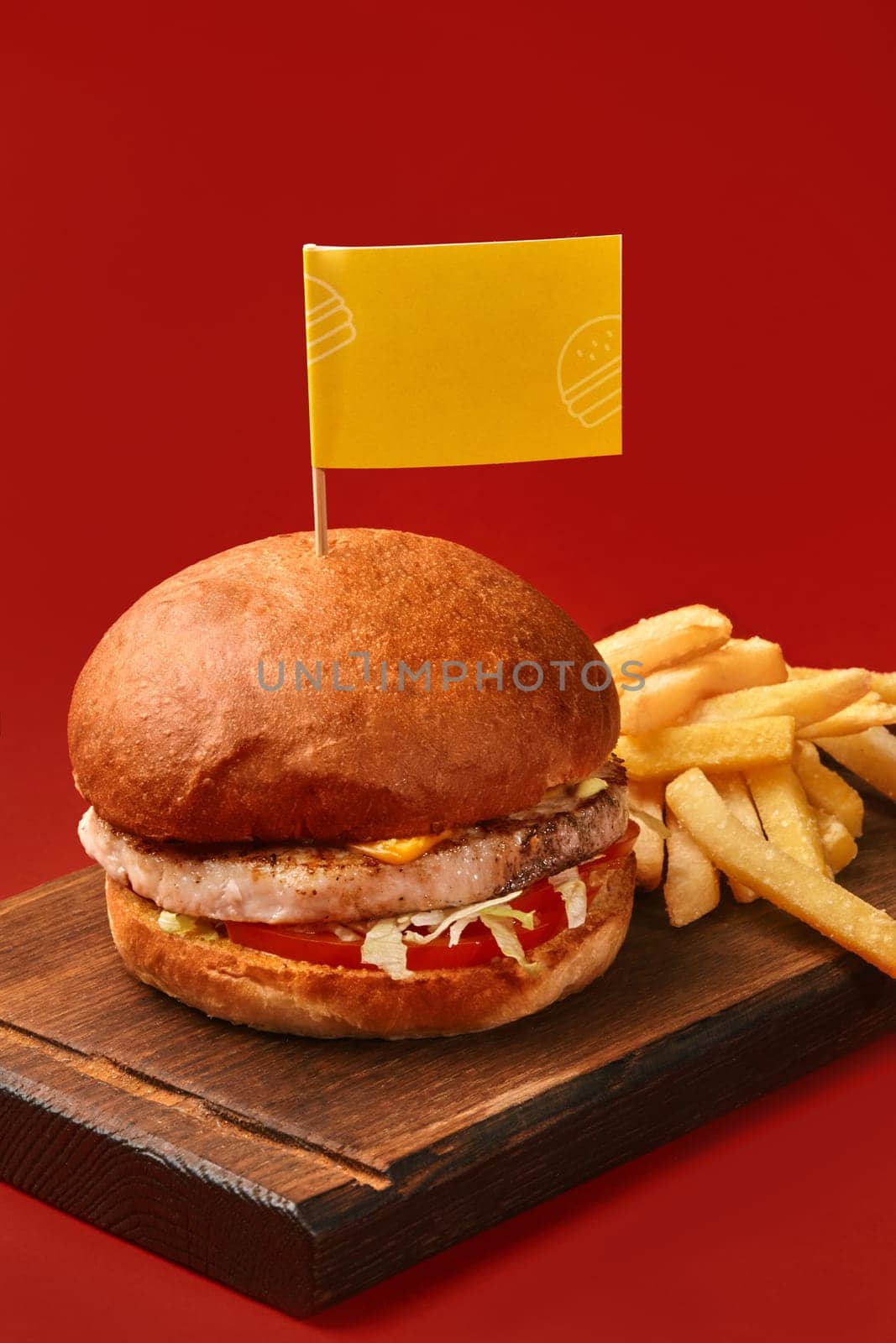 Tasty burger with meat, cheese, salad, tomato and french fries on wooden board is waiting to be eaten