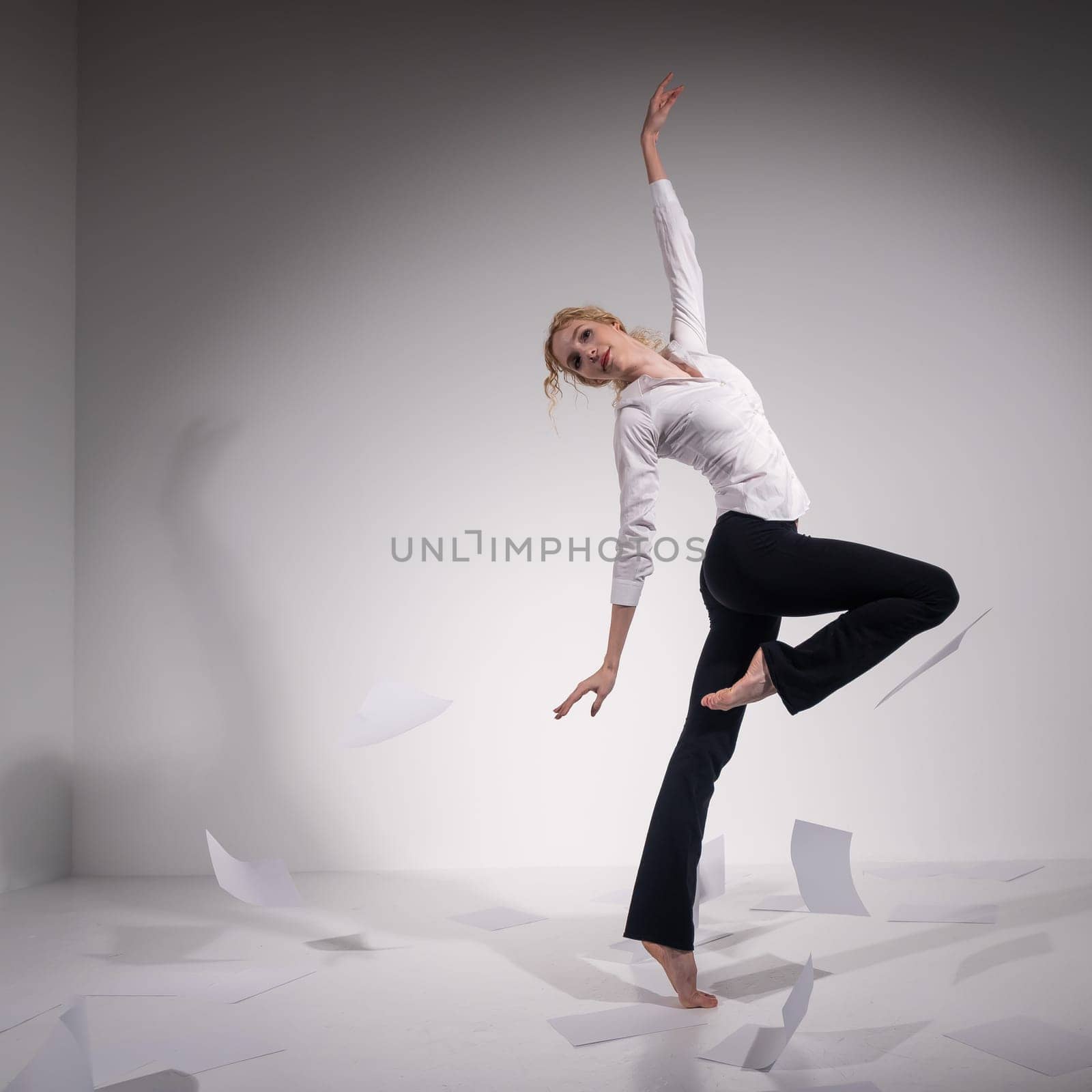 A graceful ballerina in a business suit throws documents. Business woman dance barefoot on a white background.