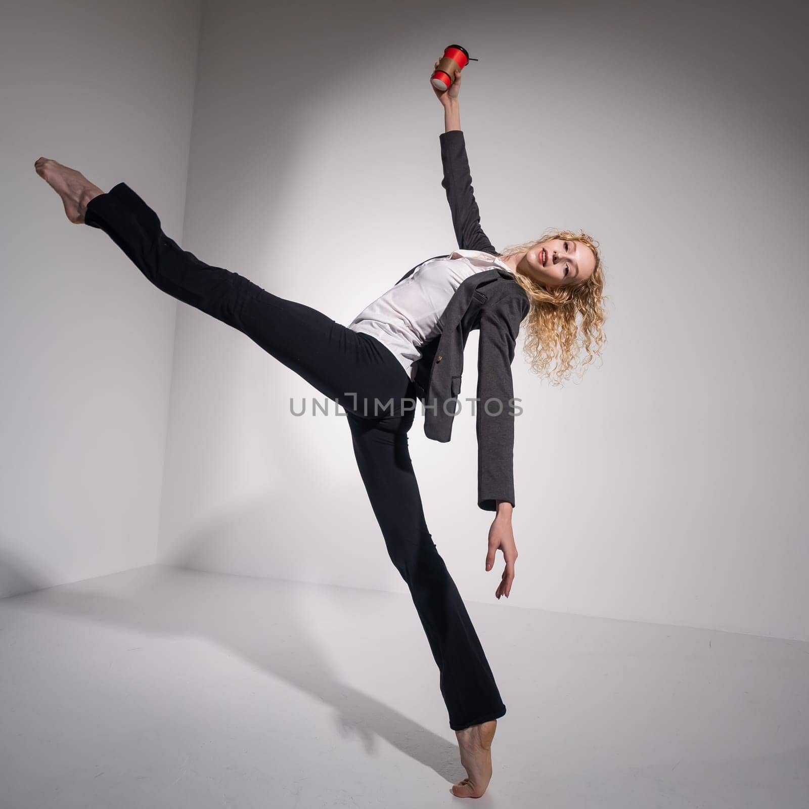 Barefoot ballerina in business suit dancing with a cup of coffee on a white background