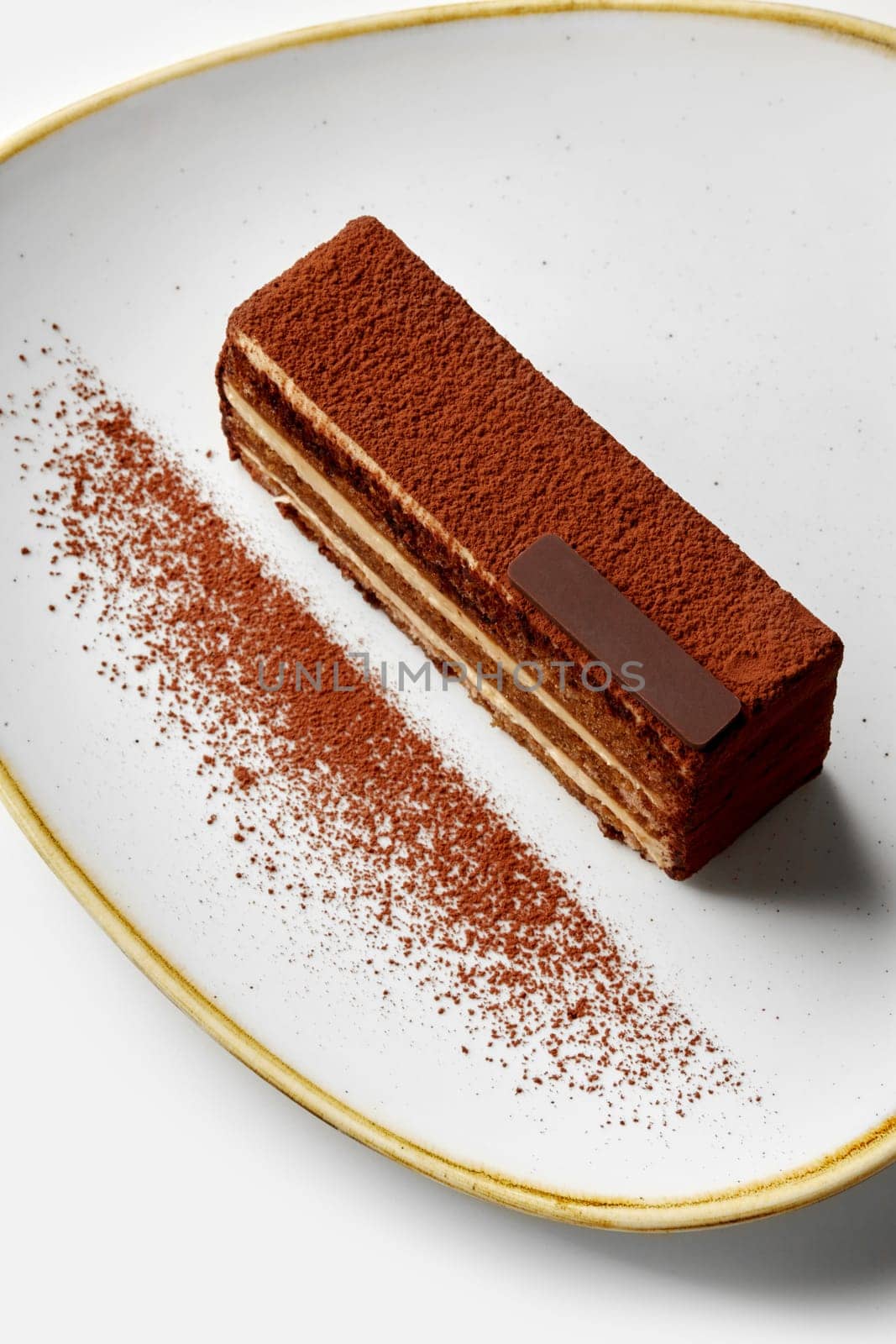 Freshly made tiramisu cake presented on a white plate, dusted with cocoa powder, creating an enticing visual for dessert lovers