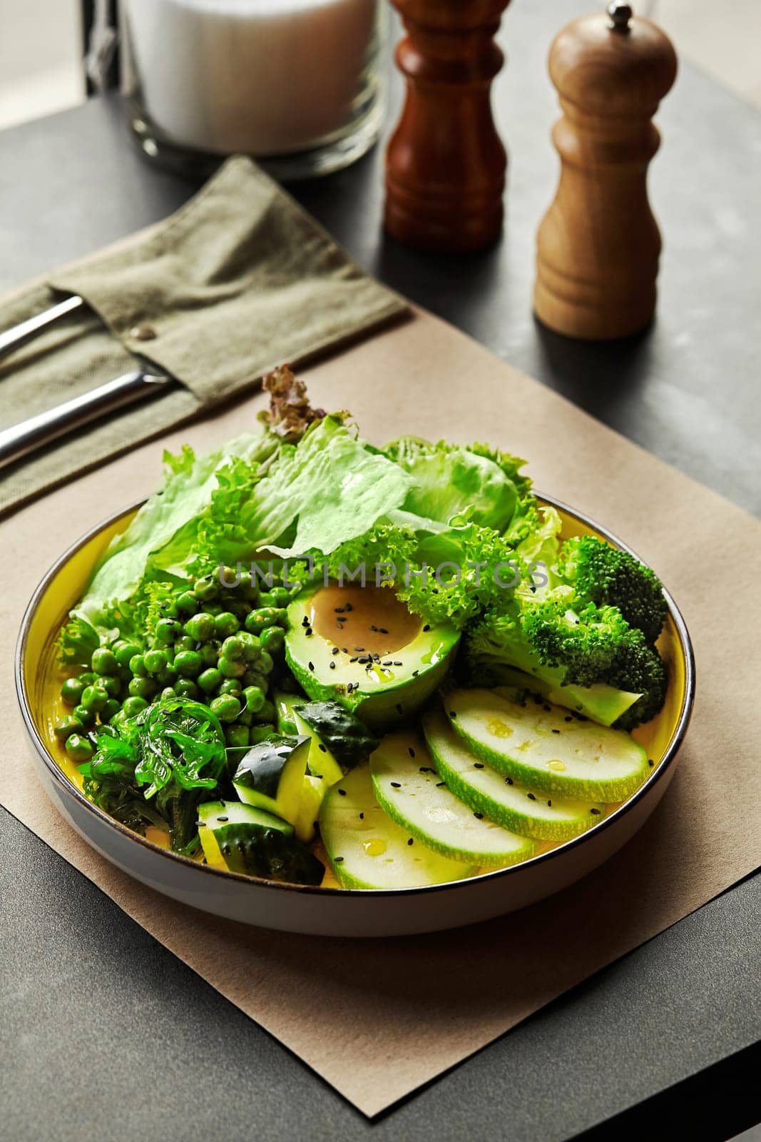 Healthy green vegan buddha bowl with avocado, broccoli, peas, zucchini, wakame seaweed and lettuce leaves, seasoned with black sesame seeds and olive oil