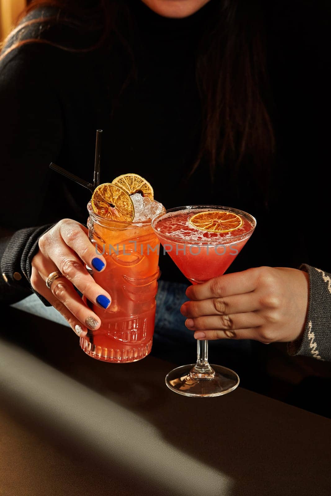 Woman enjoying refreshing cocktails with orange garnish in a tiki glass and martini glass