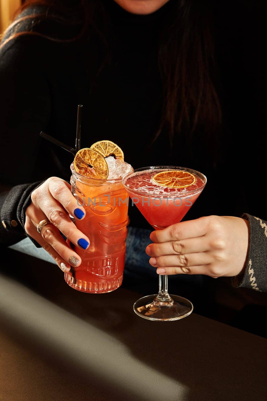 Woman enjoying two refreshing cocktails garnished with dried oranges, one served in a tiki mug and the other in a martini glass