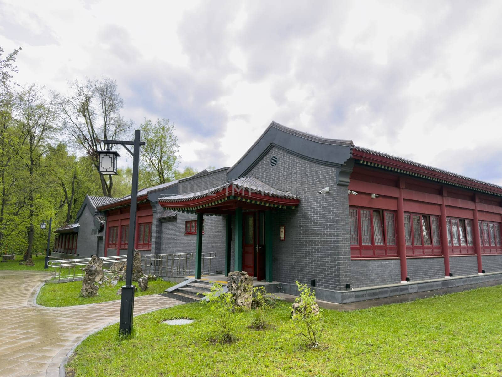 Moscow, Russia, April 25, 2025: Chinese style building with decorative red windows and gray tiled roof located in Huamin Park surrounded by spring greenery and traditional lanterns