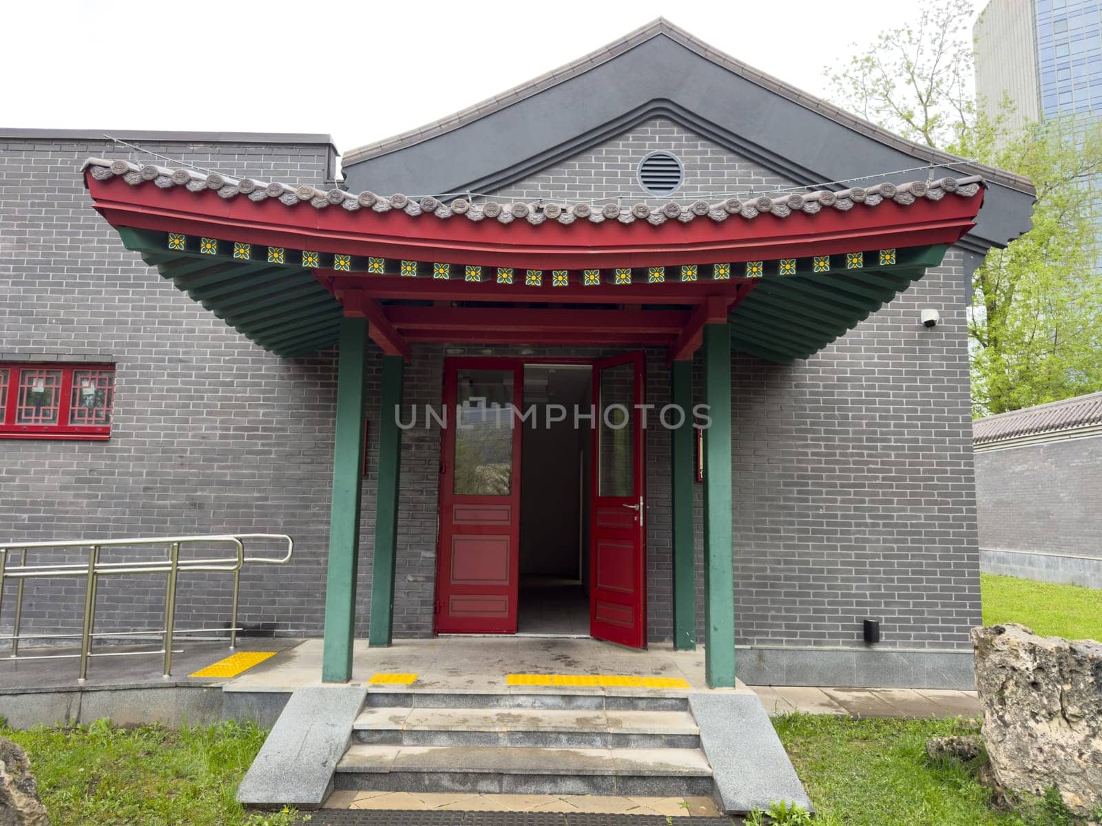 Moscow, Russia, April 25, 2025: Entrance to Chinese style building in Huamin Park with open red doors, traditional roof tiles, tactile paving and accessible ramp for inclusive public access