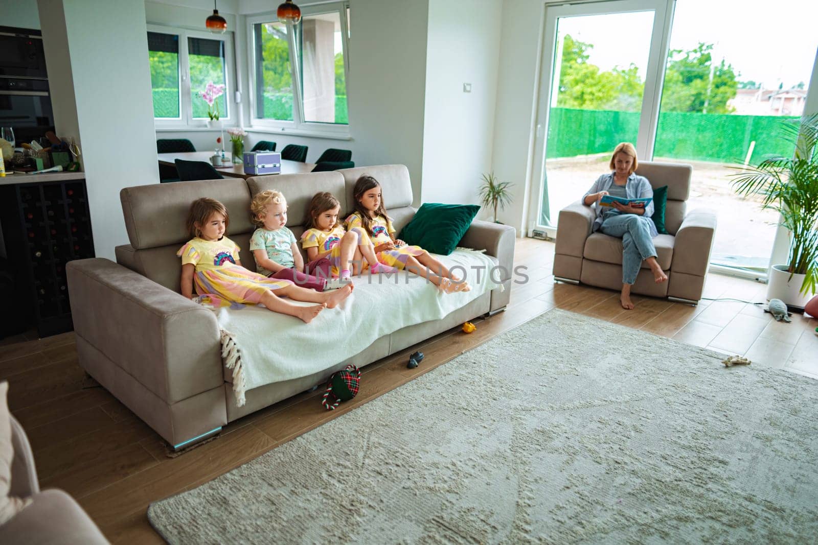 Four children relax on a sofa while an adult reads nearby.