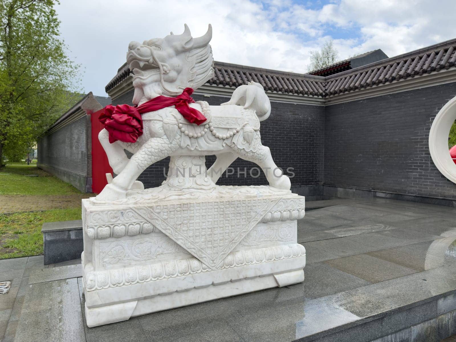 Moscow, Russia, April 25, 2025: White qilin sculpture with red ceremonial ribbon decorates entrance to Chinese style complex in Huamin Park, showcasing traditional symbol of prosperity and protection