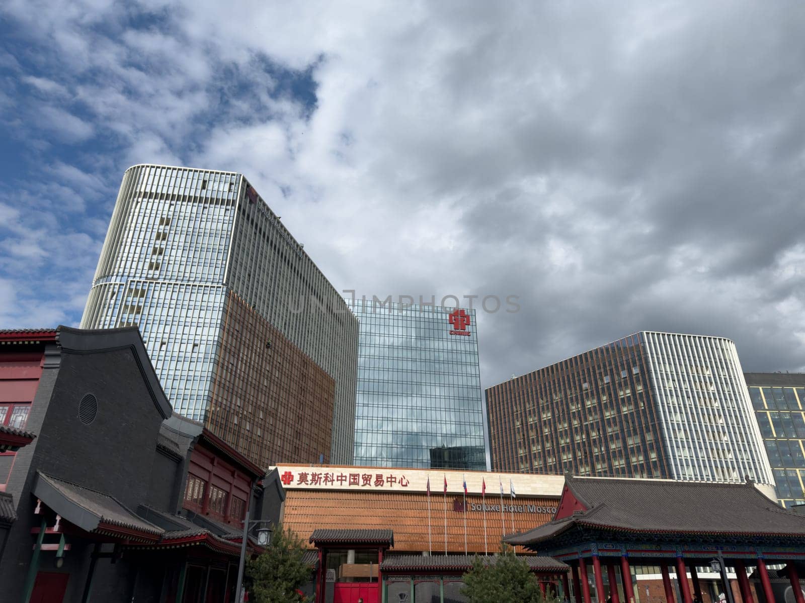 Moscow, Russia, April 25, 2025: Modern glass buildings of Chinese Trade Center and Soluxe Hotel Moscow rise above traditional Chinese style architecture in urban landscape near Huamin park