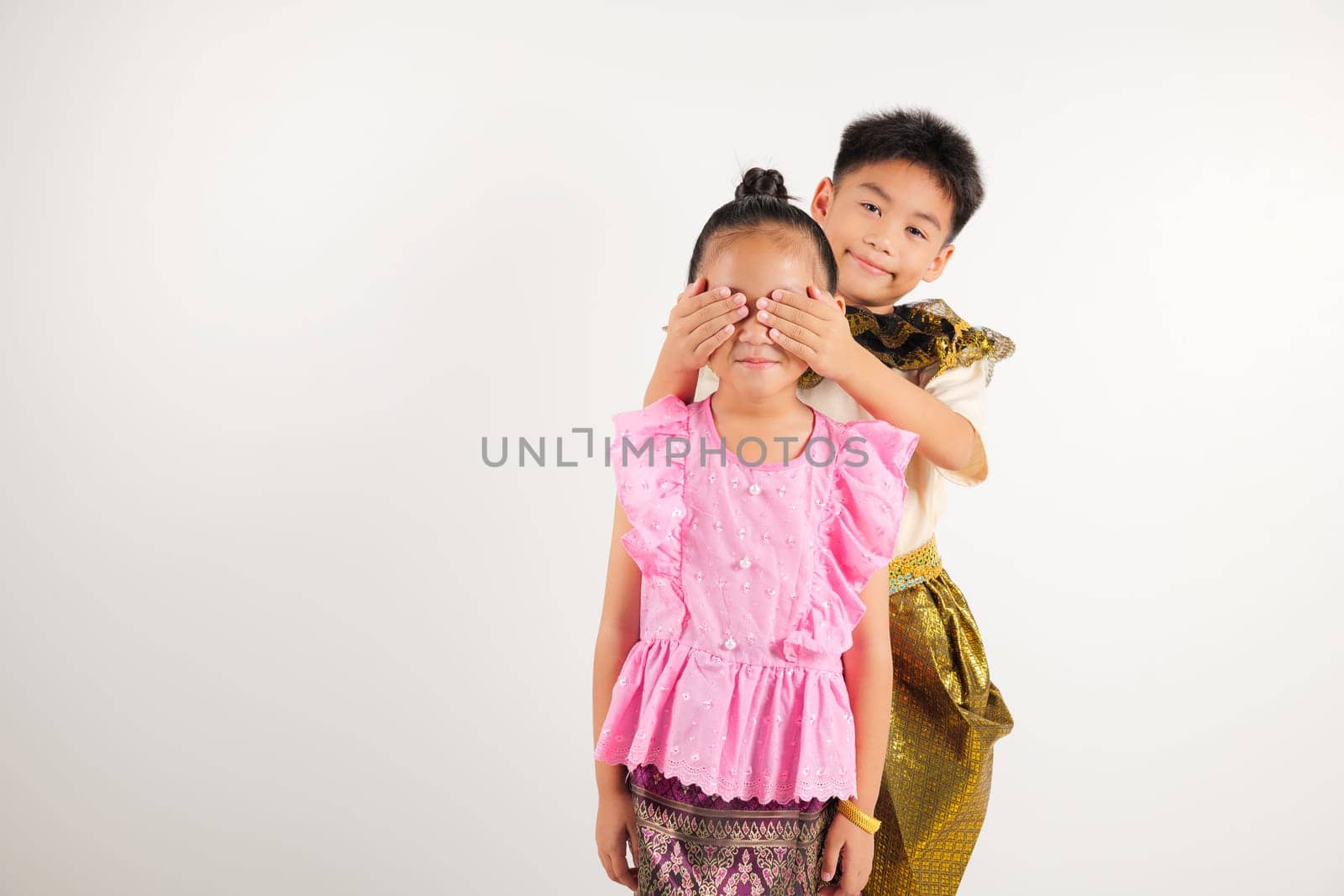Portrait Thailand kid girl and boy traditional Thai dress costume together close eyes with hands play guess who or hide and seek studio isolated white background, Happy children hiding behind his back