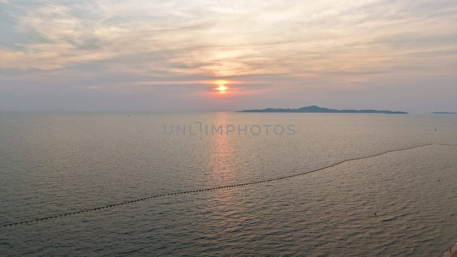Golden hues of sunset paint the sky over a tranquil ocean, its surface reflecting the light as distant islands silhouette against the horizon, creating a serene and picturesque seascape