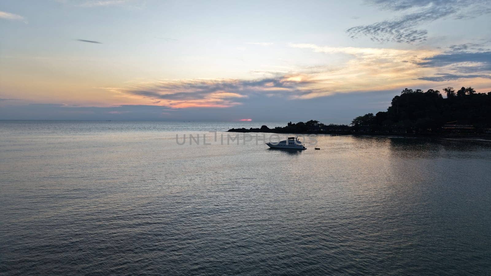 White luxury yacht rocking gently on calm ocean waters near a tropical island, with vibrant sunset hues of orange and pink reflecting on the tranquil sea