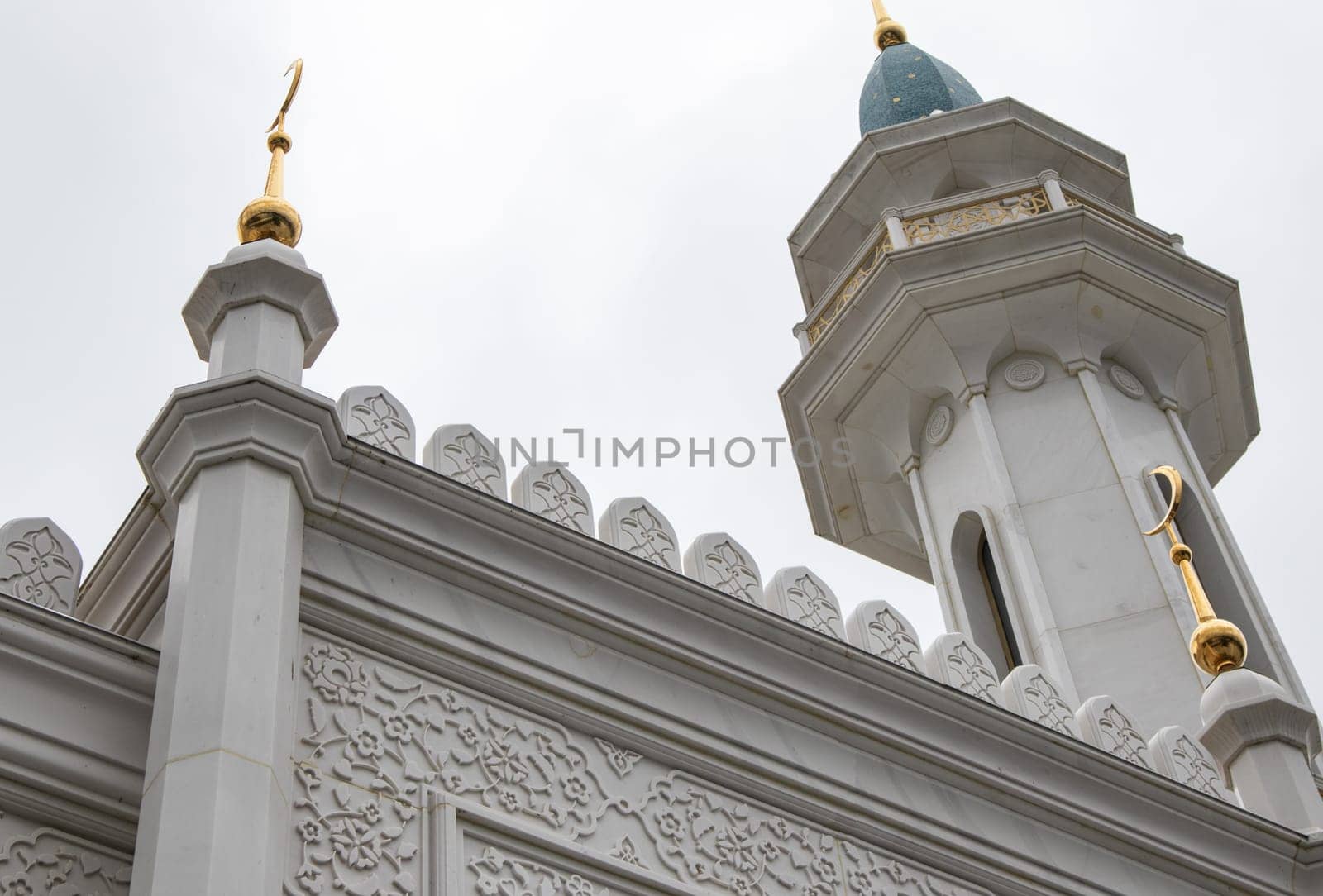 View from below the beautiful white stone minaret of the mosque with geometric patterns on the walls and crescent moon rising against the sky