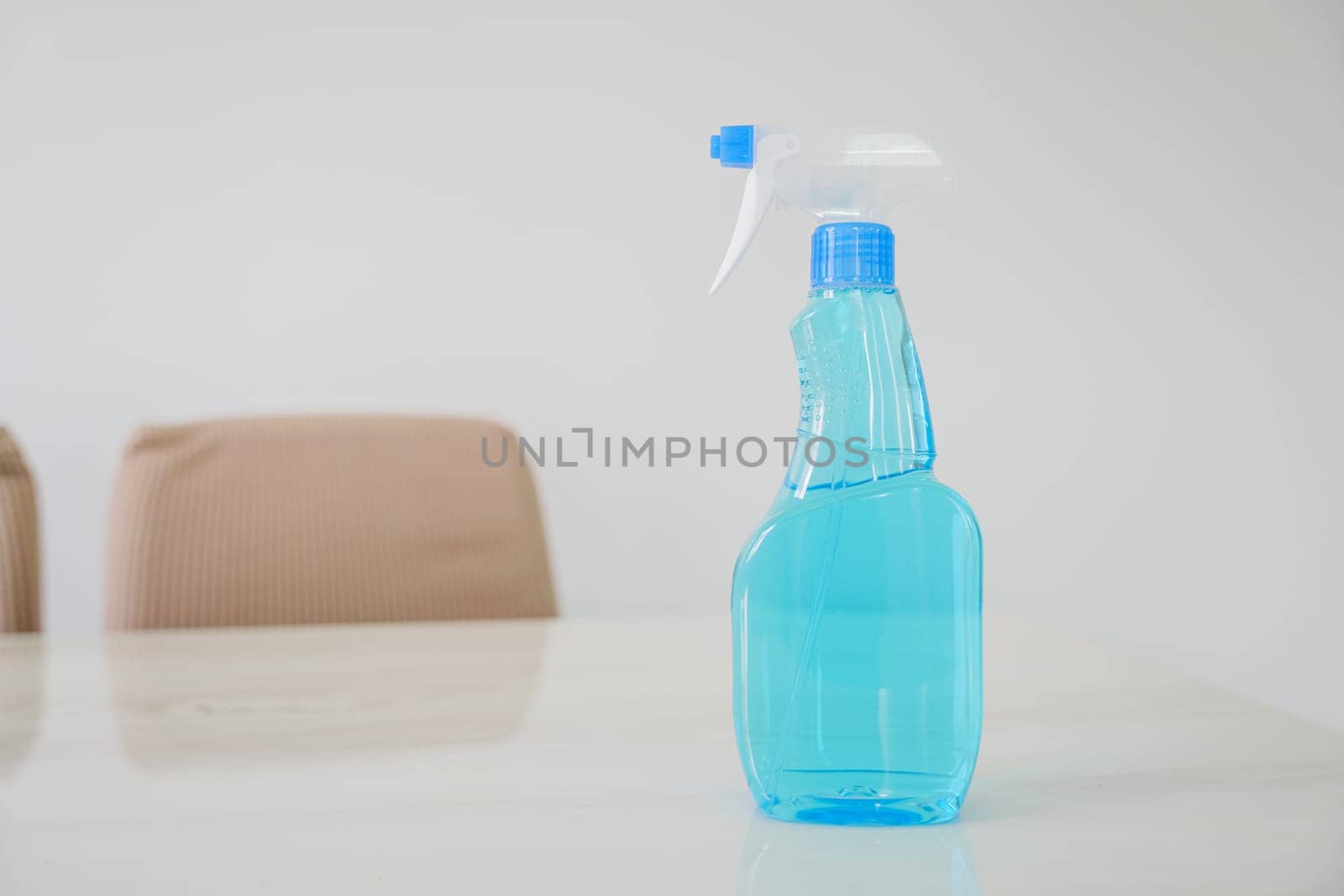 Blue glass spray bottle with white trigger in the kitchen table on a white wall background. The bottle is filled with clear blue liquid, Cleaning concept