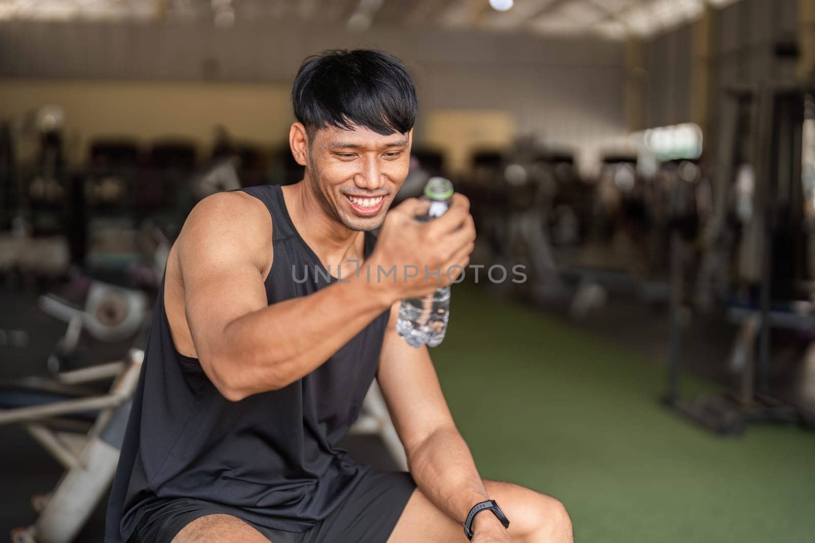 A man in a gym smiling while drinking water, showcasing the importance of hydration in fitness.