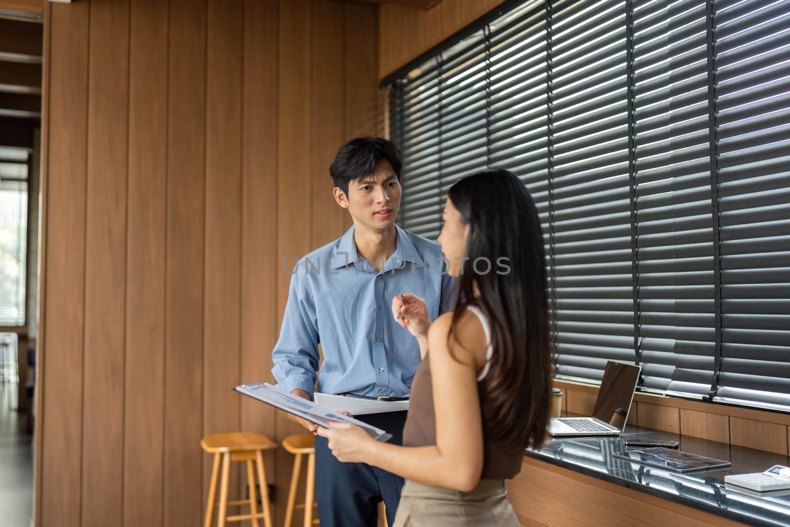 A businessman and businesswoman are engaged in a discussion, collaborating on project details in a contemporary office setting.