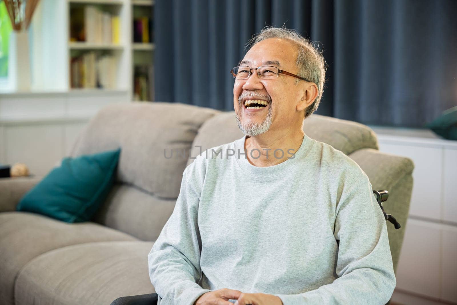 Portrait Asian old man alone relaxing on comfortable couch in cozy living room at home, happy smiling positive older senior male laughing at funny joke and thinking about good future