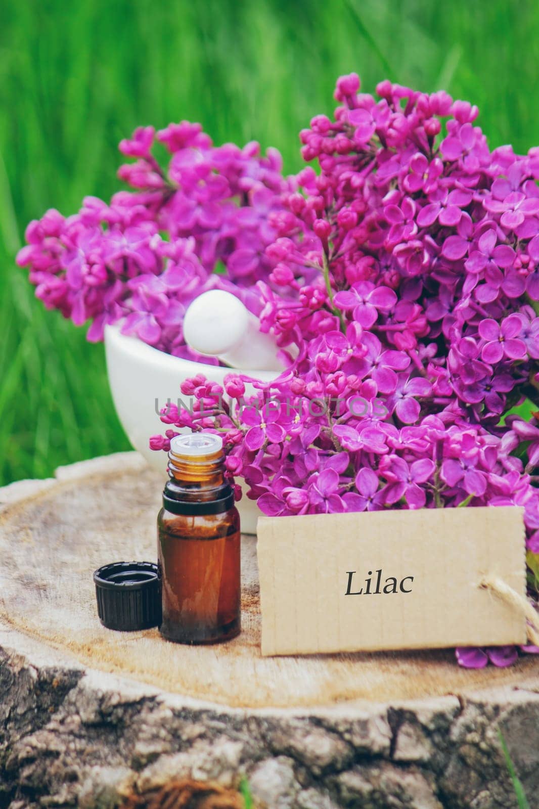 Lilac essential oil on a wooden stump. Bottle with aromatic oil and lilac flowers.