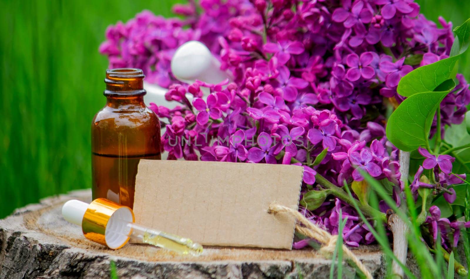 Lilac essential oil on a wooden stump. Bottle with aromatic oil and lilac flowers.