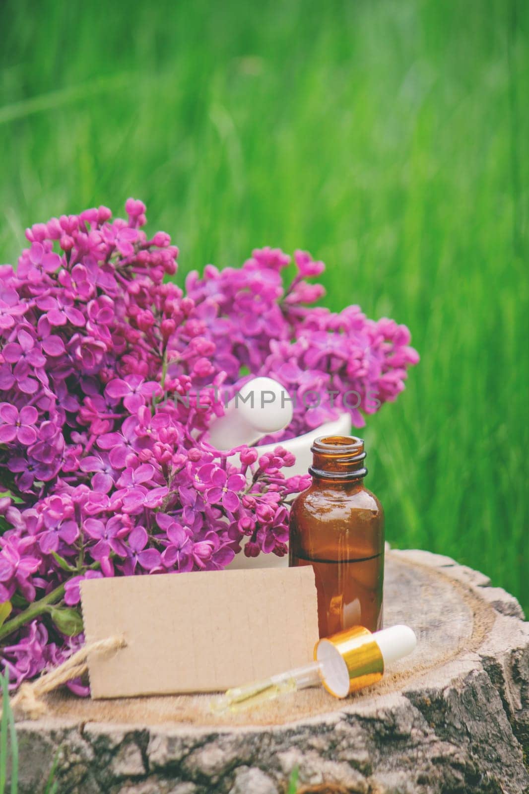 Lilac essential oil on a wooden stump. Bottle with aromatic oil and lilac flowers.