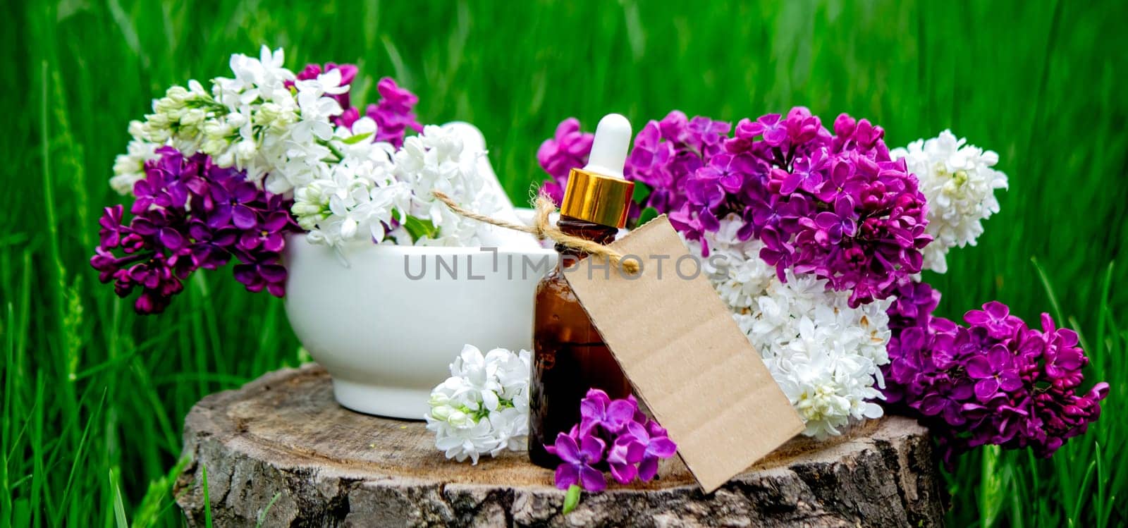 Lilac essential oil on a wooden stump. Bottle with aromatic oil and lilac flowers.