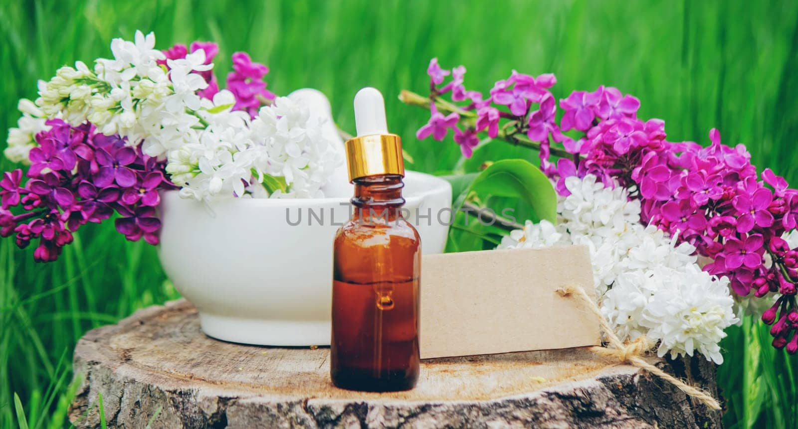 Lilac essential oil on a wooden stump. Bottle with aromatic oil and lilac flowers.