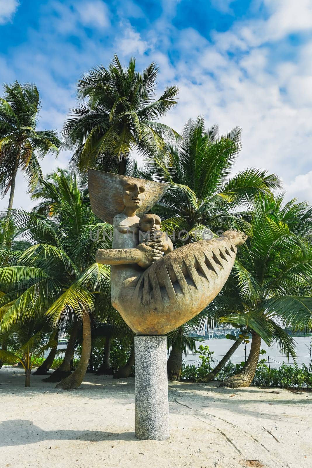 Singapore, Singapore - 4 April 2025: "Mother and Child statue by Dr Ng Eng Teng at Gardens by the Bay, standing amidst palm trees with sandy ground under sunny skies with clouds