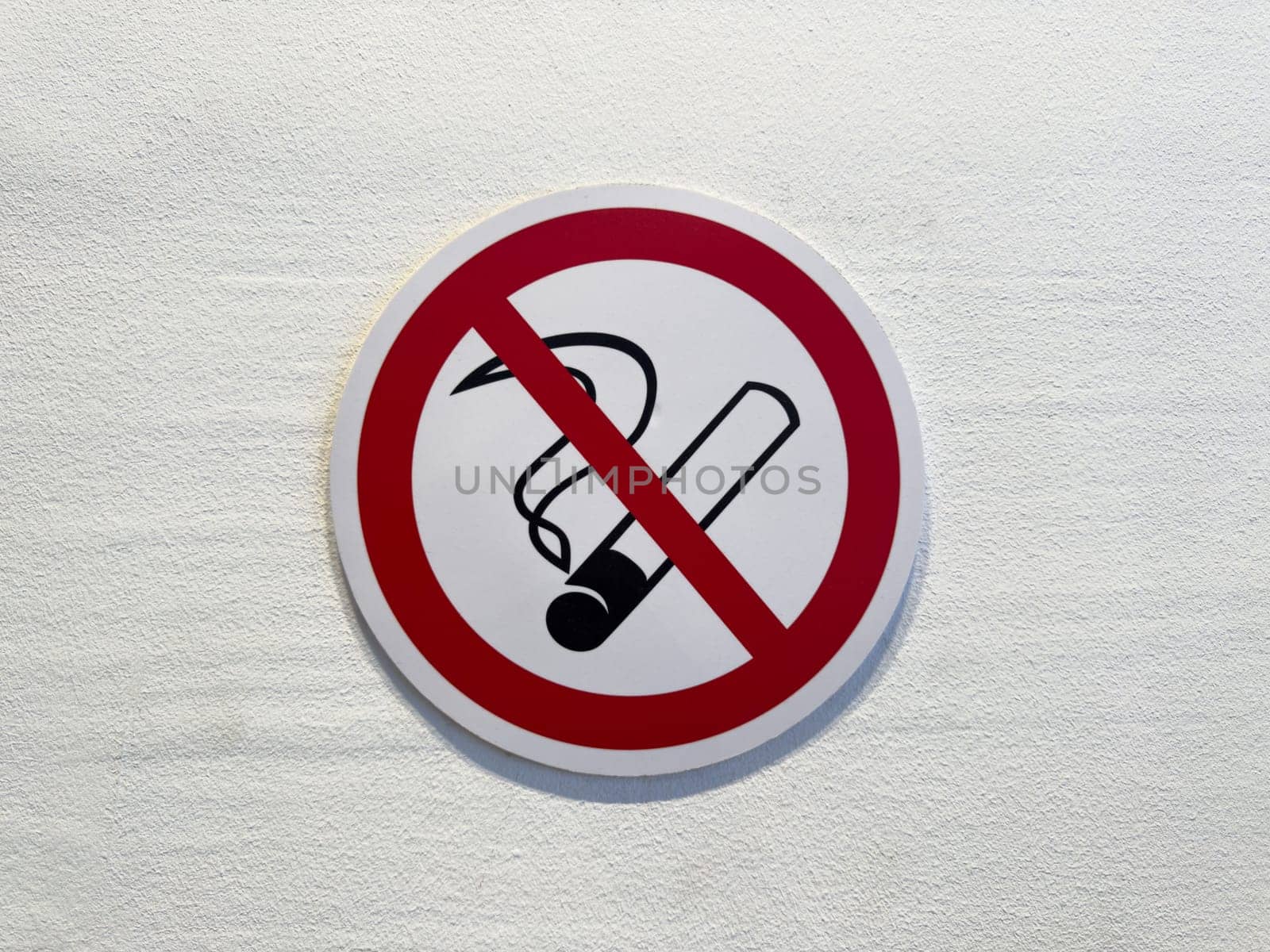 Close up of no smoking sign on white wall. Red circle with cigarette symbol and diagonal line emphasizes public health, safety and clean air in indoor environments