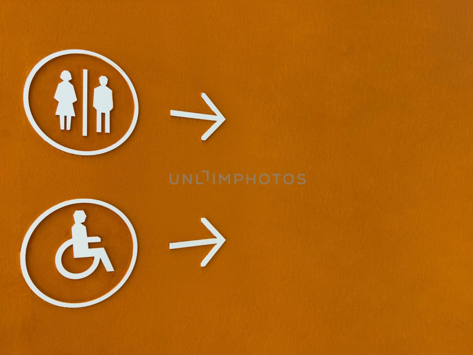 Modern restroom direction sign with male, female and wheelchair symbols on bold orange wall, pointing to the right. Accessible and inclusive design for public facilities navigation