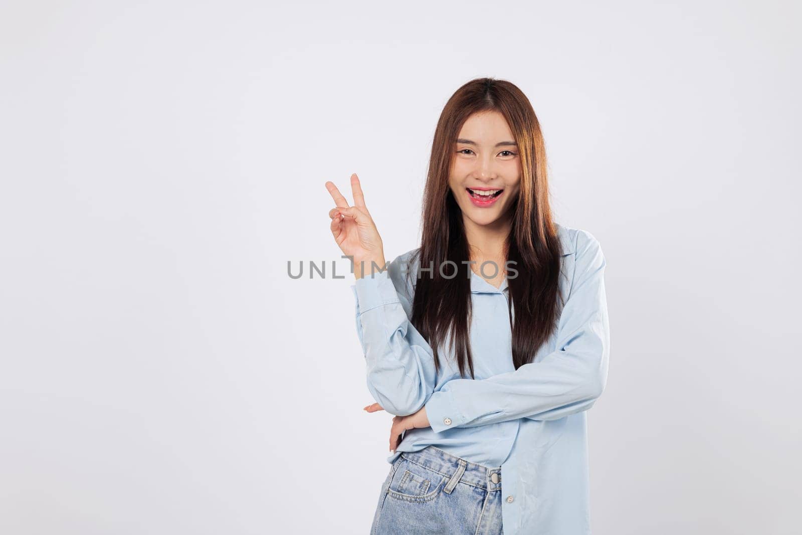 Victory sign and positive energy shine through as an Asian woman shows a gesture of victory with two fingers. Her optimistic smile brings out excitement and happiness.