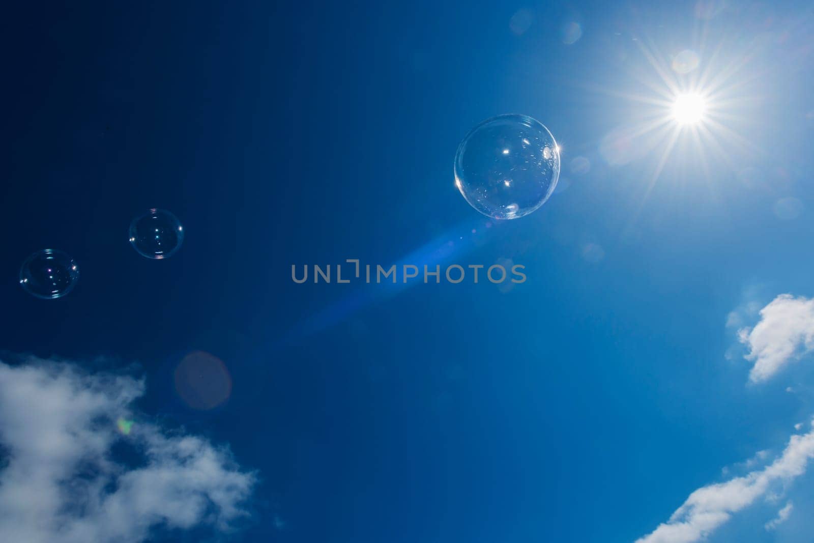 Soap bubbles in the blue sky with isolated clouds backlit by the sun.