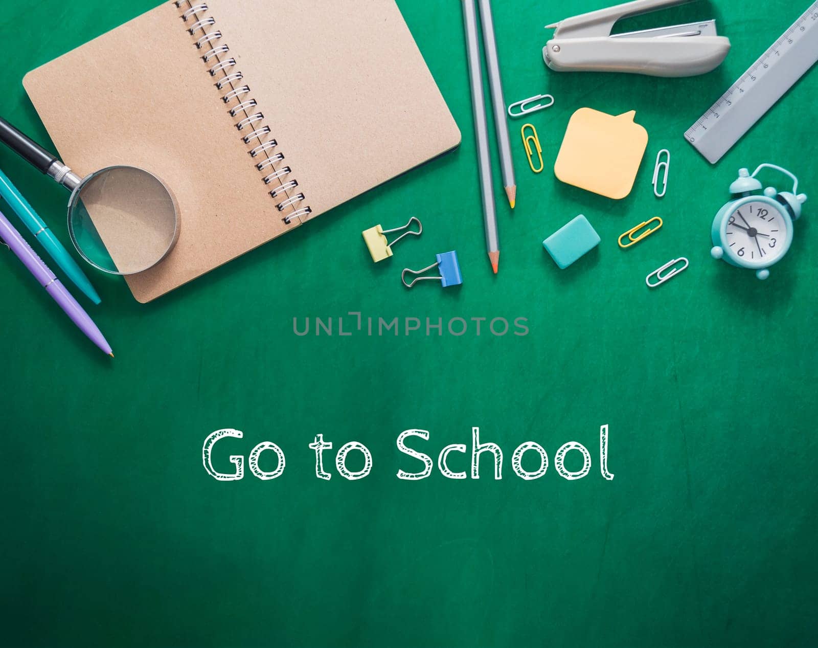 Green notebook with a magnifying glass and a clock on it. The words go to school are written on the notebook