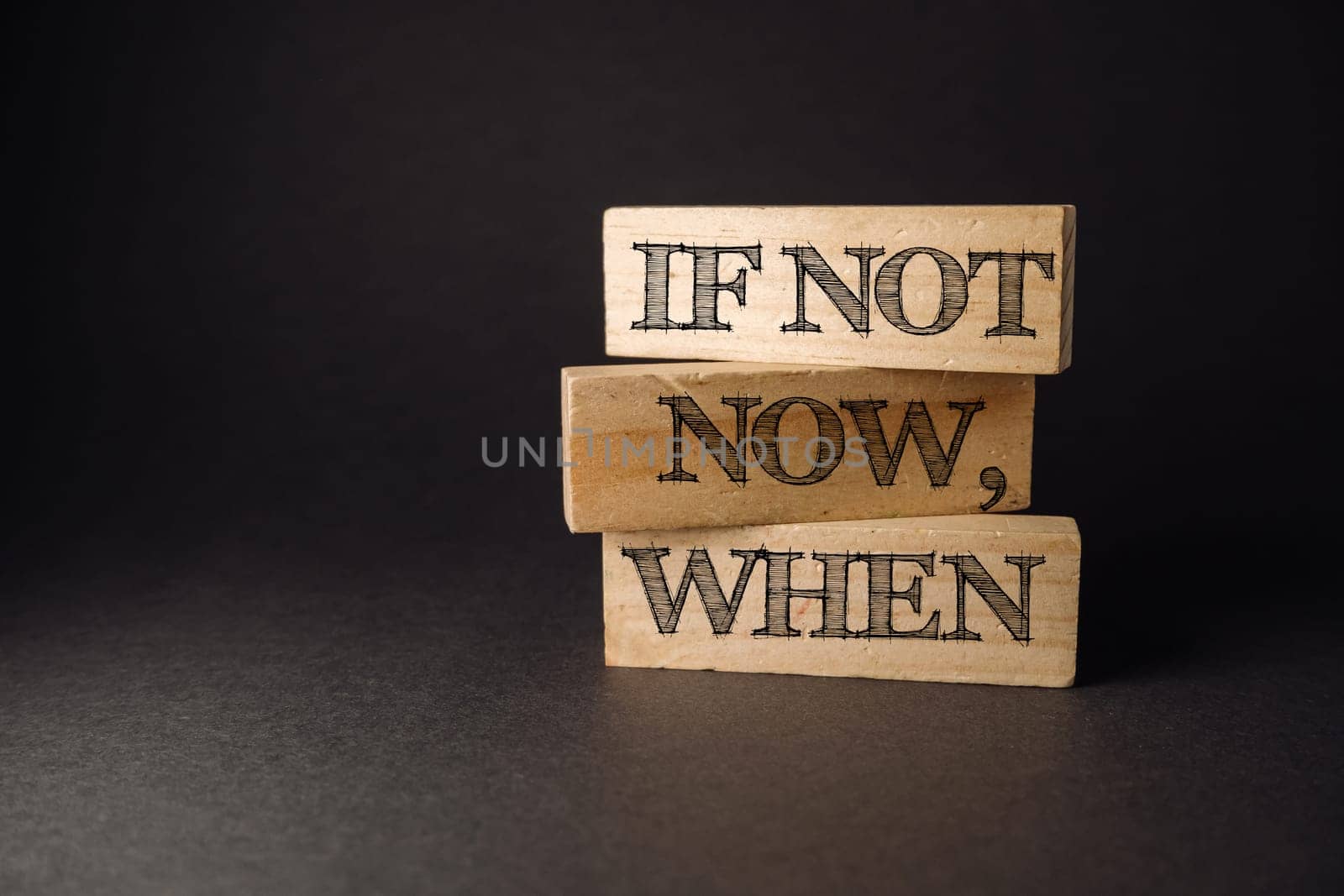 Three wooden blocks with the words if not now when written on them. The blocks are stacked on top of each other