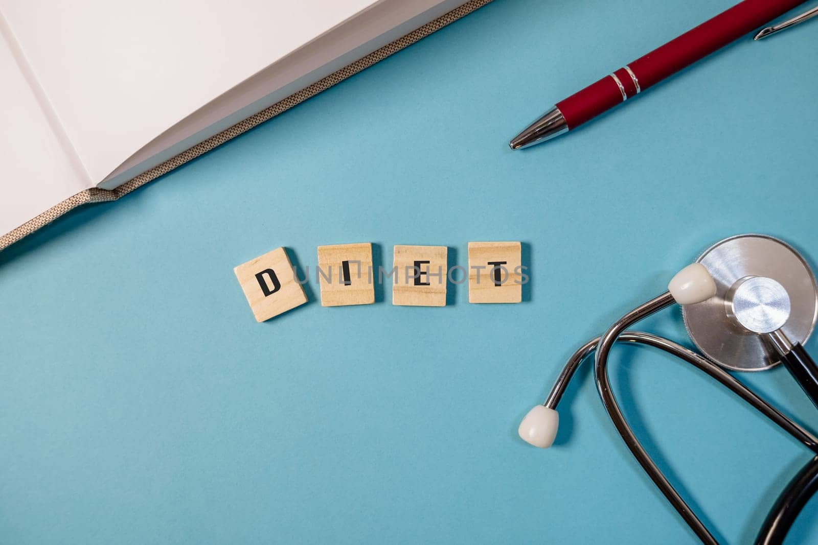 Blue background with a pen and a stethoscope. The word diet is written in wooden blocks on the table