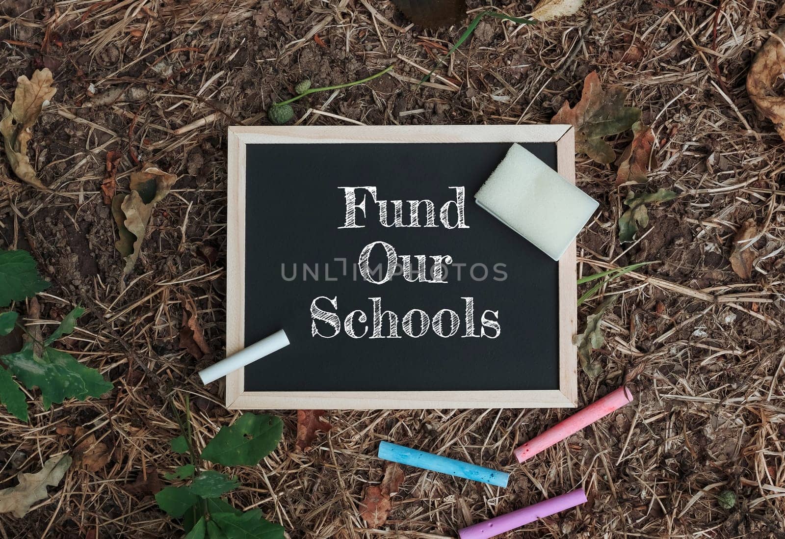 Chalkboard with the words fund Our Schools written on it. There are also some crayons on the ground
