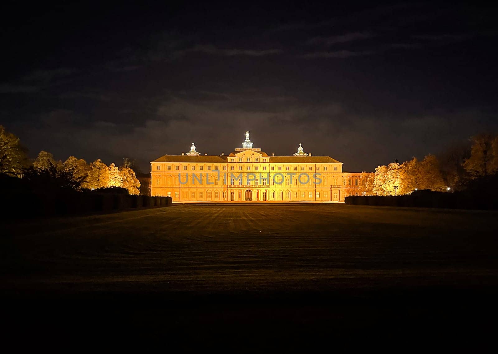 Large building with a clock tower is lit up at night. The building is surrounded by a grassy field