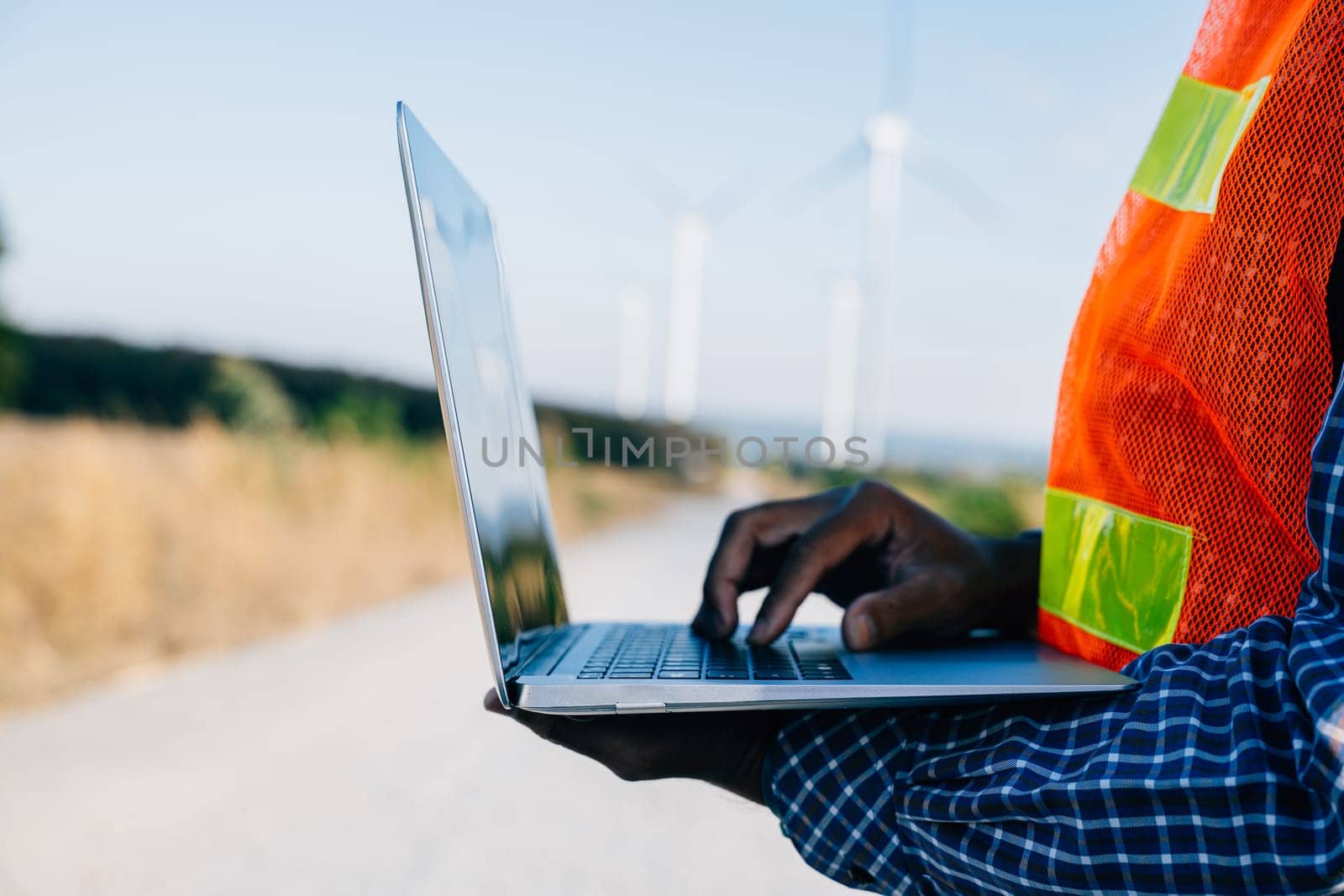 Technician with laptop by windmills an engineer at work. Service technician ensures turbine efficiency. Confident in landscape development focused on windmill service and quality.