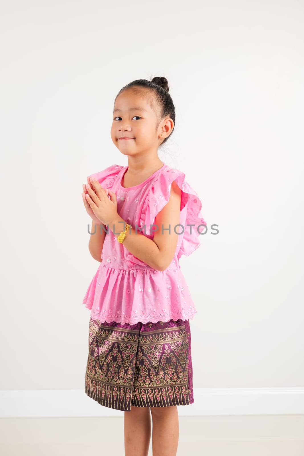 Portrait of Thailand kid girl smiling traditional Thai dress costume posing to pay respect in studio shot isolated white background, Happy kindergarten child sawasdee symbol or welcome