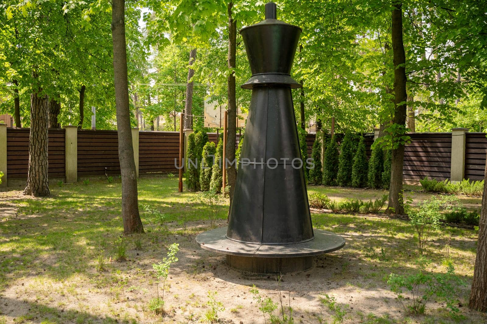 Bench in the park in the form of a chess piece in the park. Park with tall trees, green lawn on a sunny day