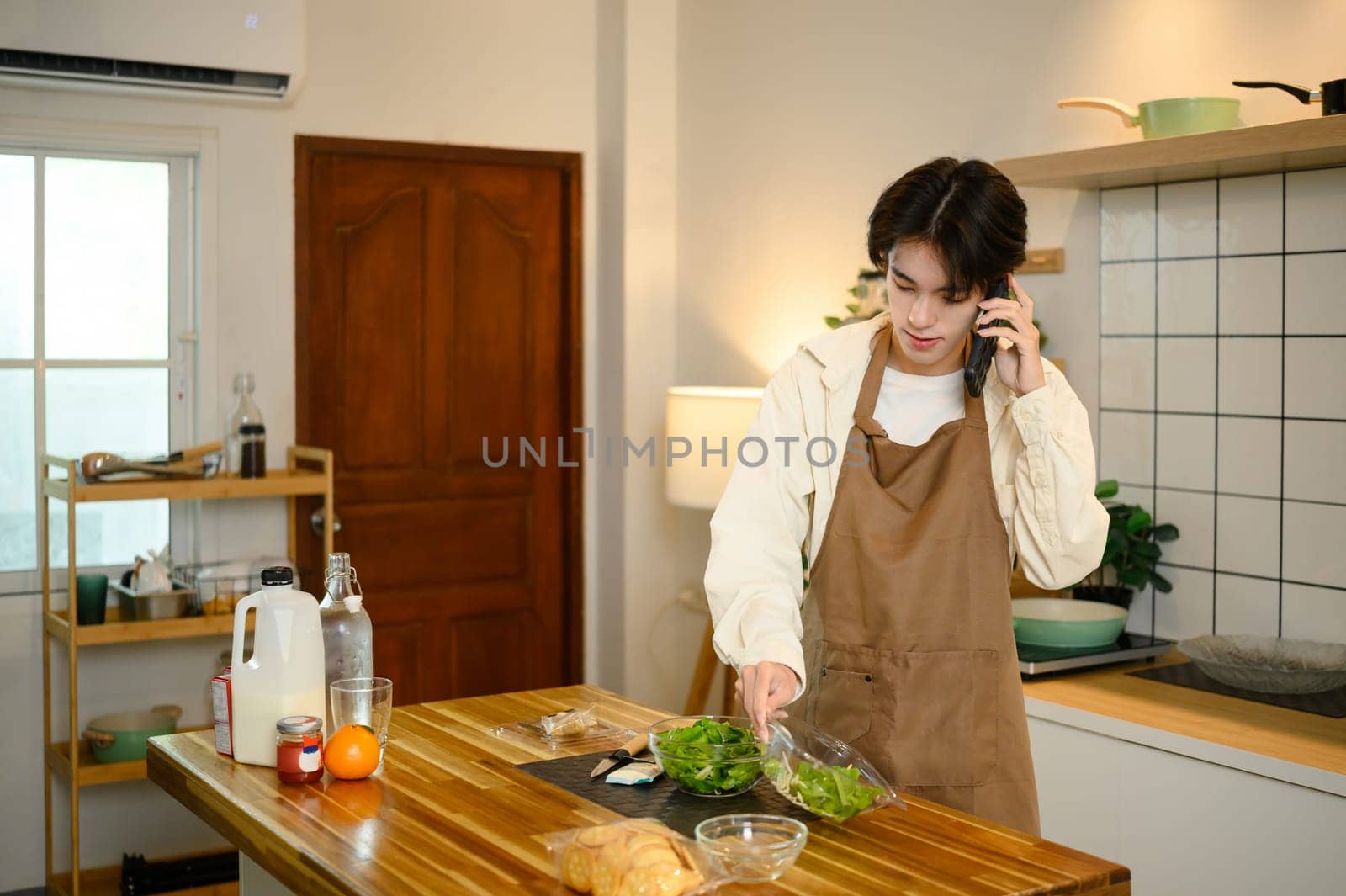 Young man talks on the phone while making a fresh green salad at home.