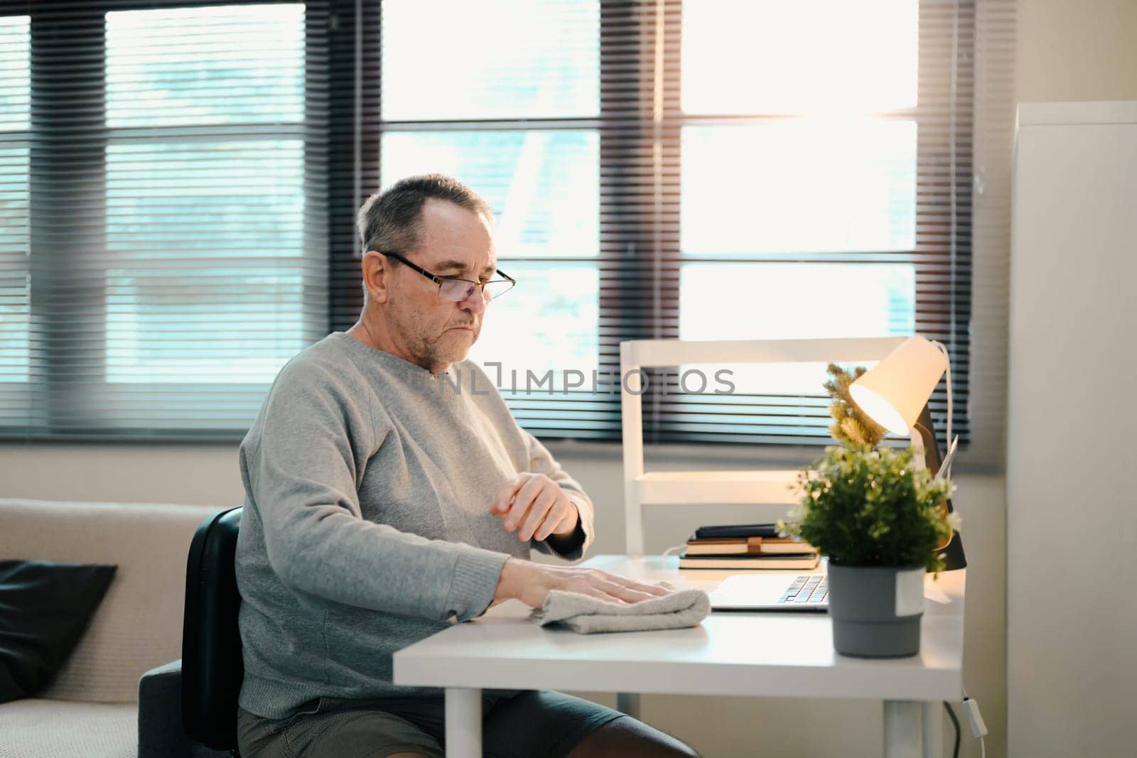 Caucasian older man in a gray sweater wipes down his white desk with a cloth.