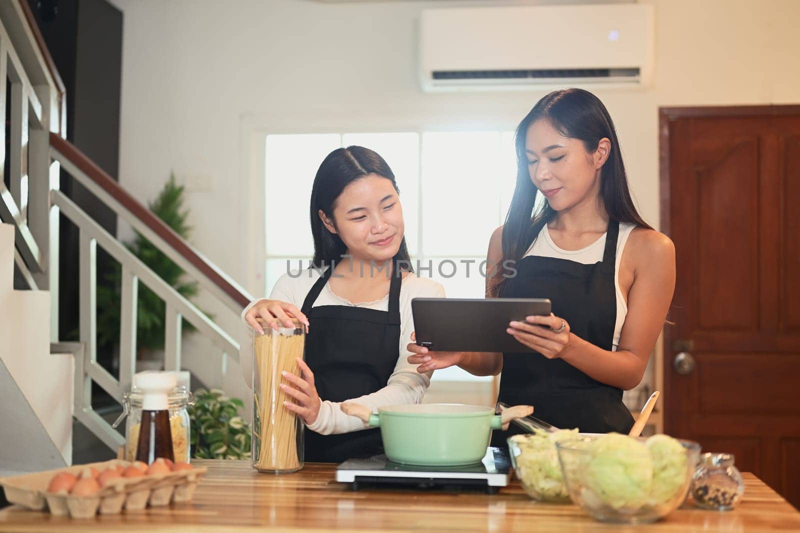 Mother and her daughter review recipe on a tablet while preparing meal in a kitchen.