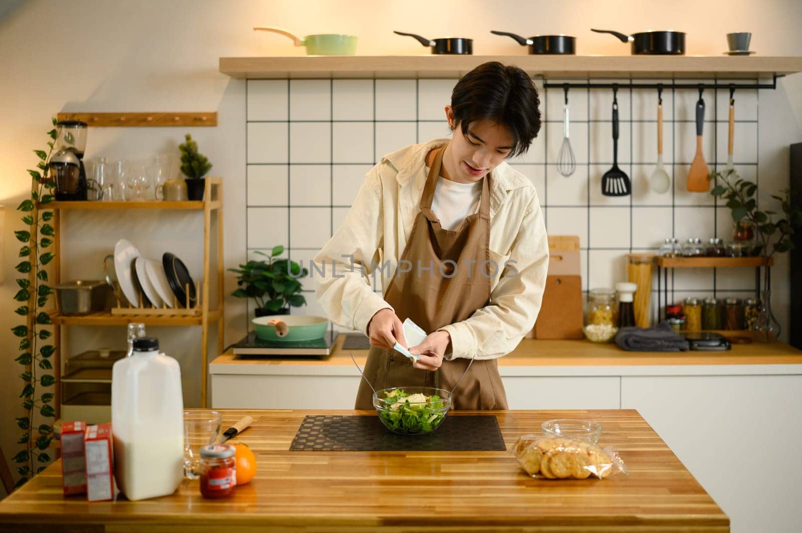Young man pours dressing onto a bowl of fresh vegetable salad.