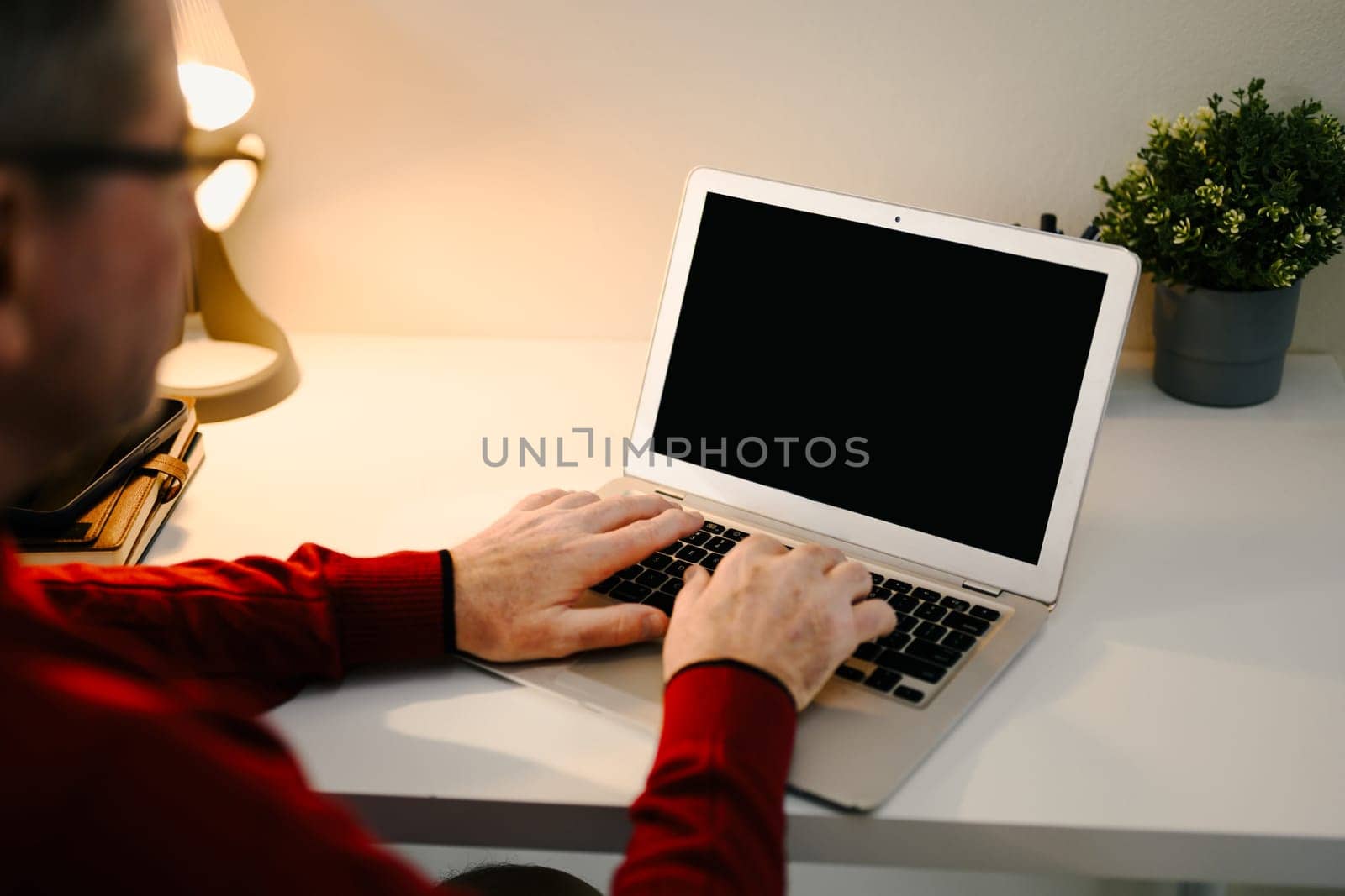 Close p of an older man hands typing on a laptop with a black screen.