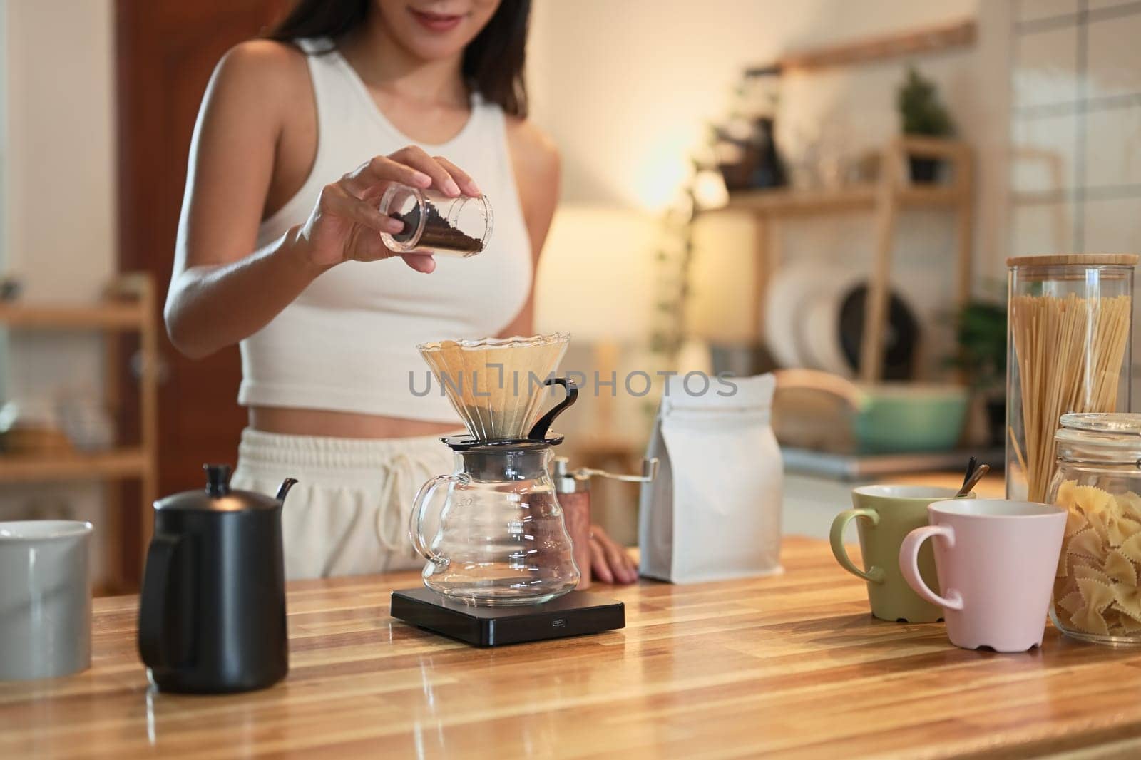 Young woman preparing pour over coffee using a glass dripper in a warmly home kitchen.
