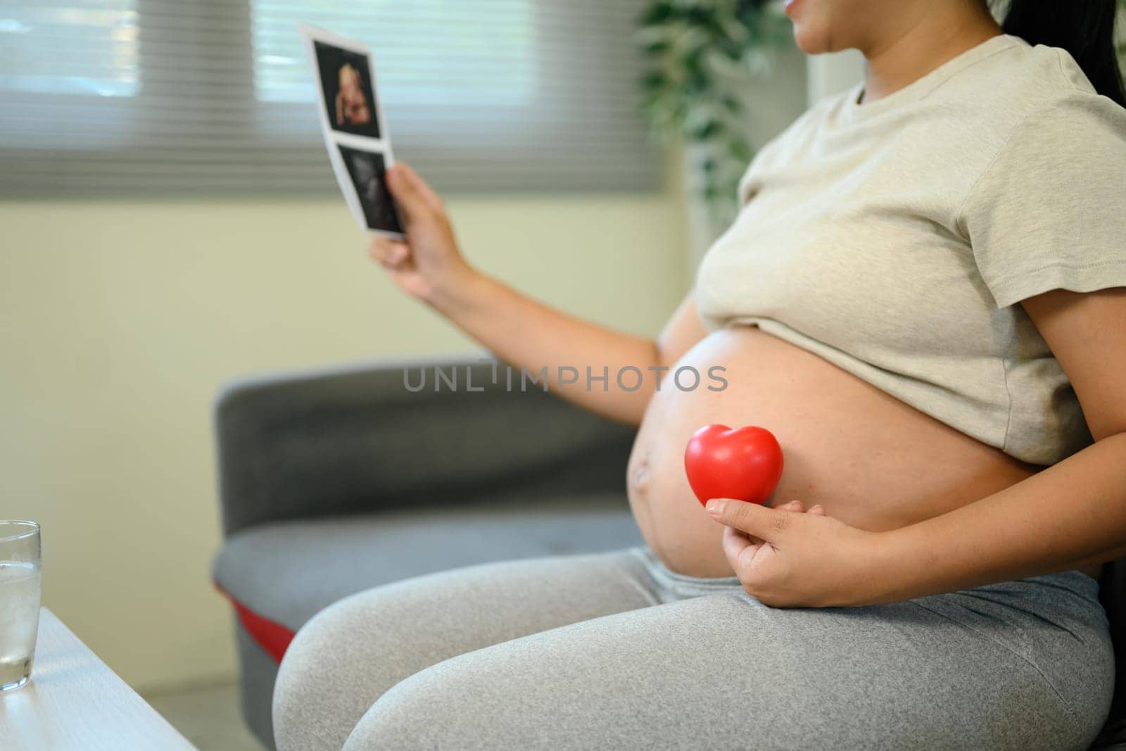 Pregnant woman holding ultrasound and red heart, maternity love and anticipation at home.